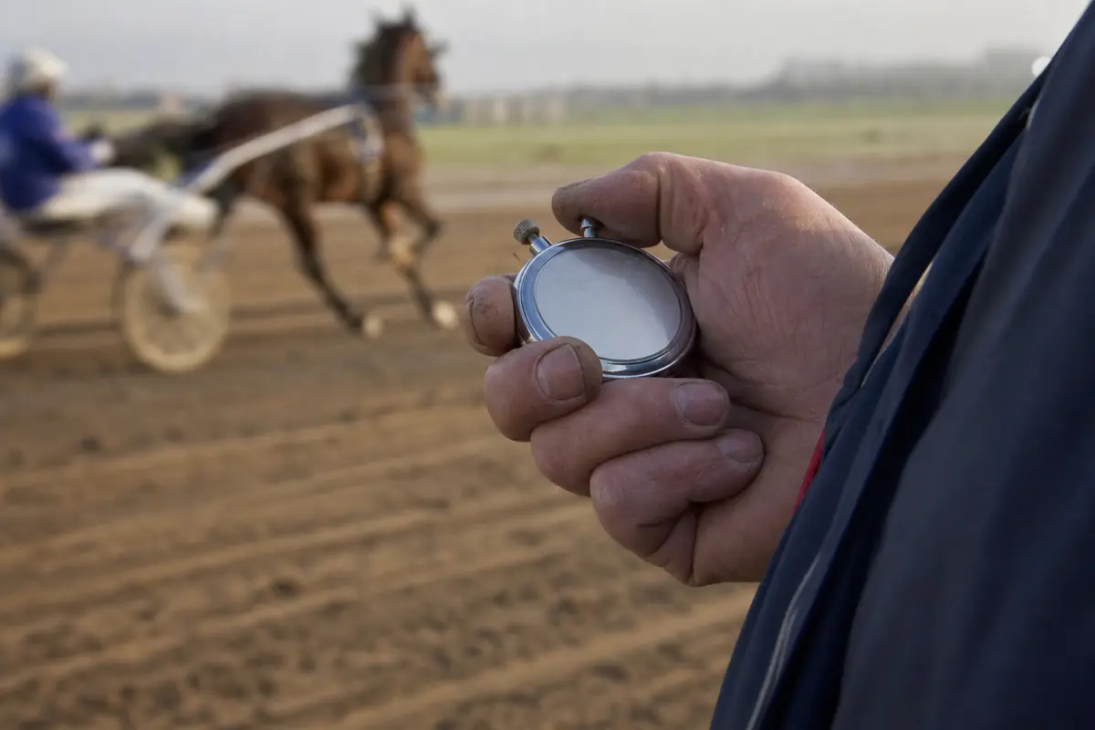 Chronomètre dans la main d'un entraîneur au bord d'une piste de trot