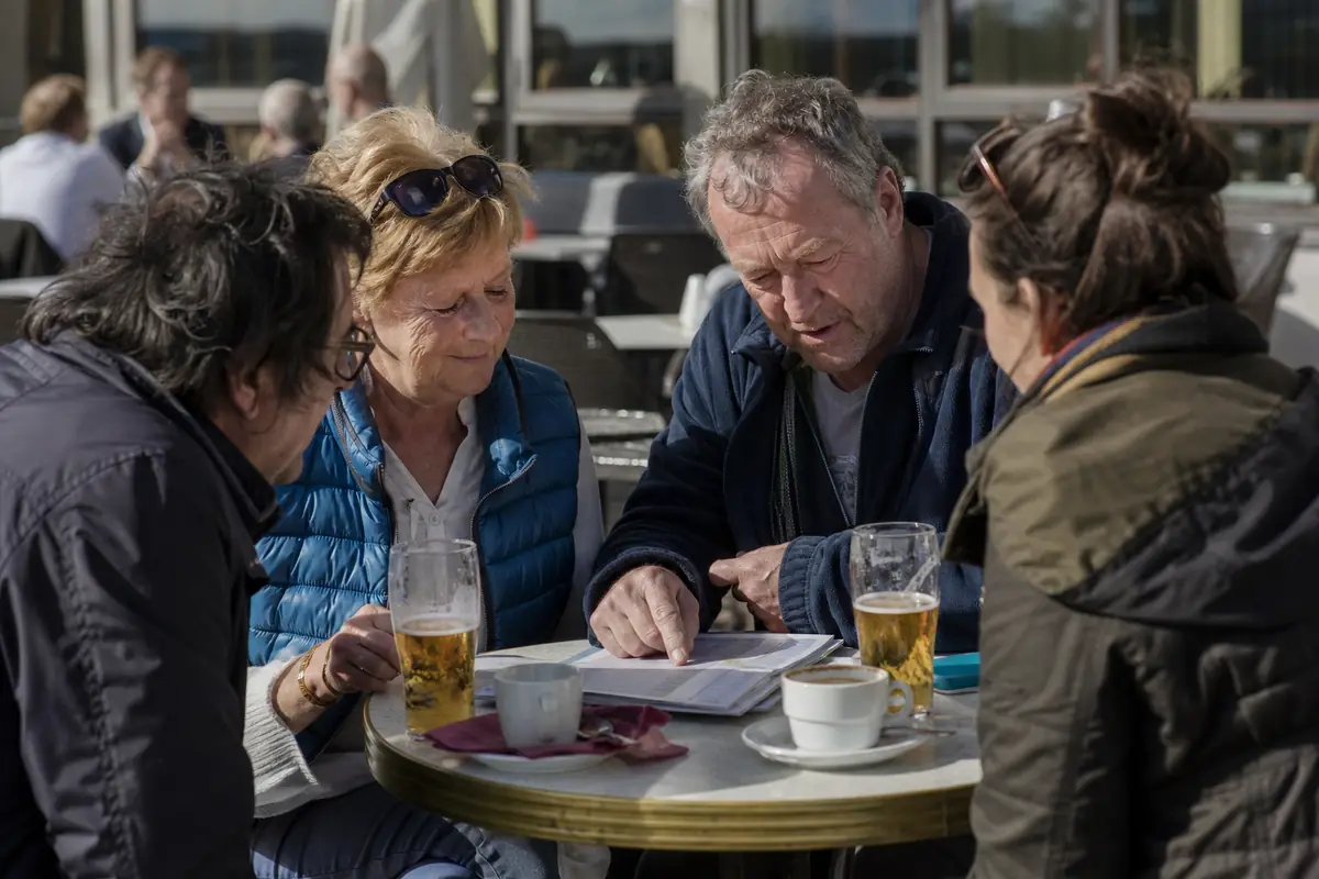 Groupe d'amis qui discutent autour d'un programme de courses en terrasse