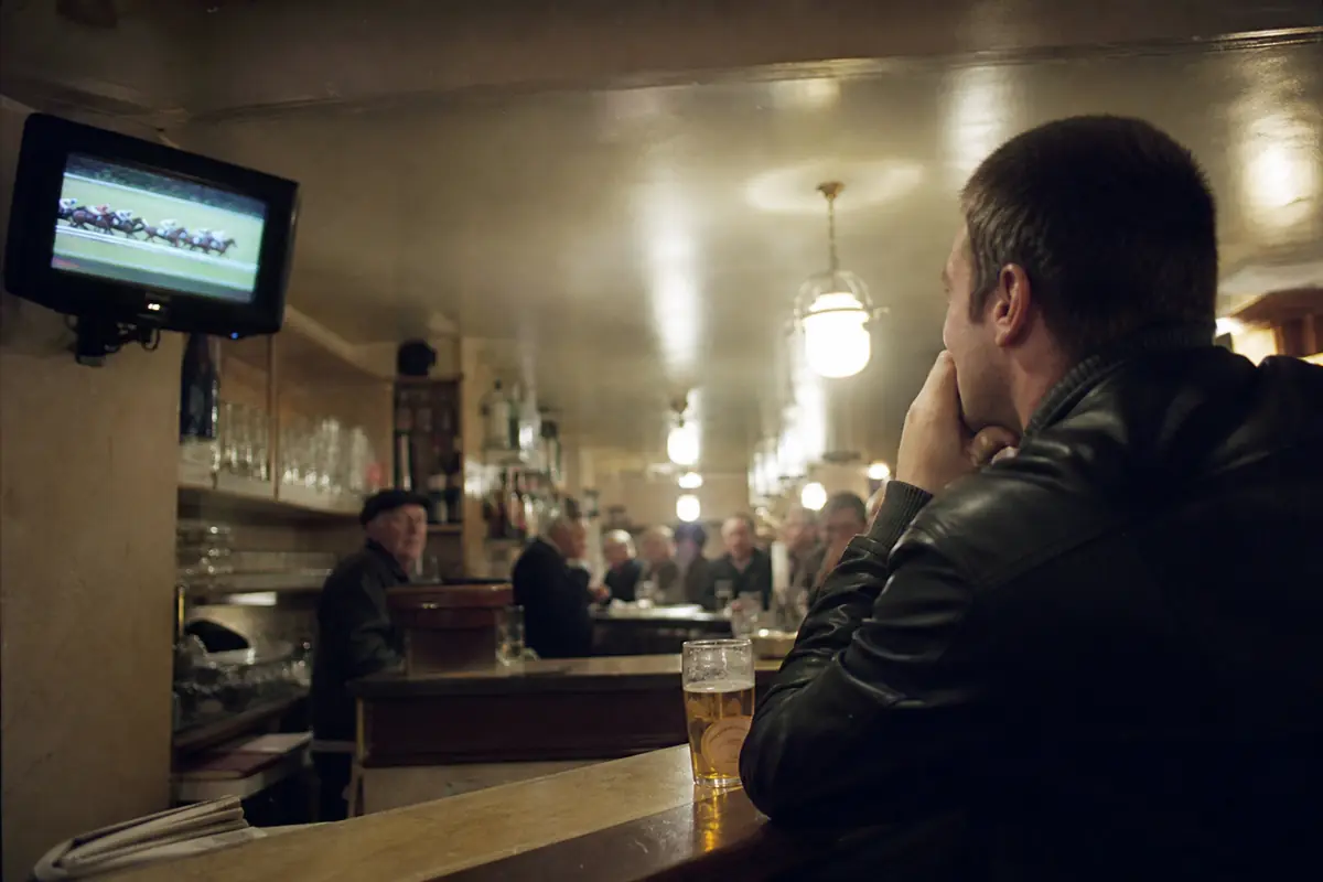 Un homme regarde une course hippique sur un écran dans un bar