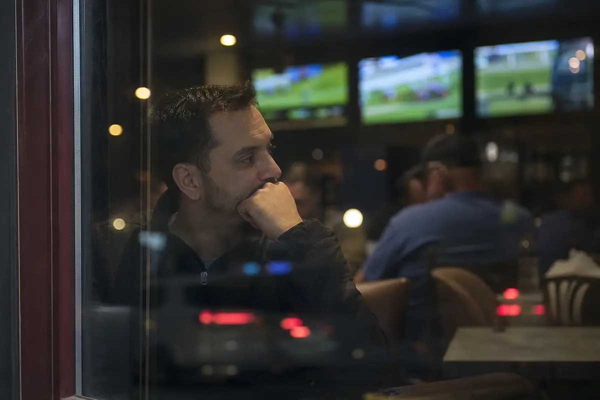 Reflet d'un homme dans une vitre avec des écrans de courses flous derrière