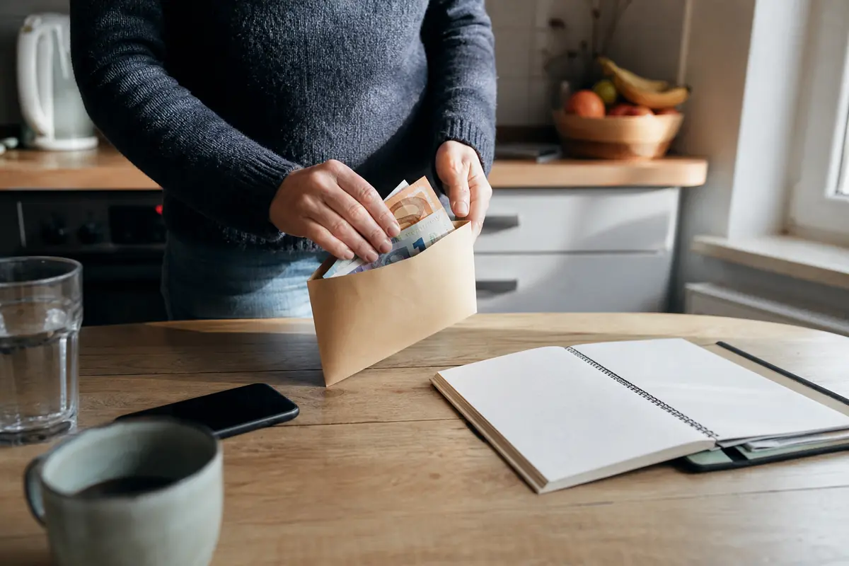 Une personne range une petite somme dans une enveloppe à part